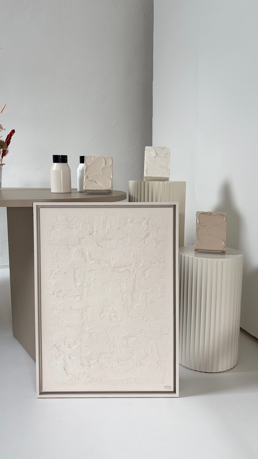 Cremefarbenes Strukturbild an einen Tisch gelehnt, mit Deko-Objekten und Trockenblumen
